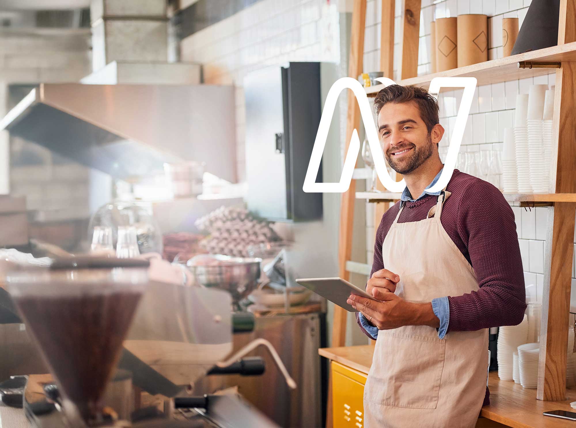 A smiling café owner holding a tablet behind the counter